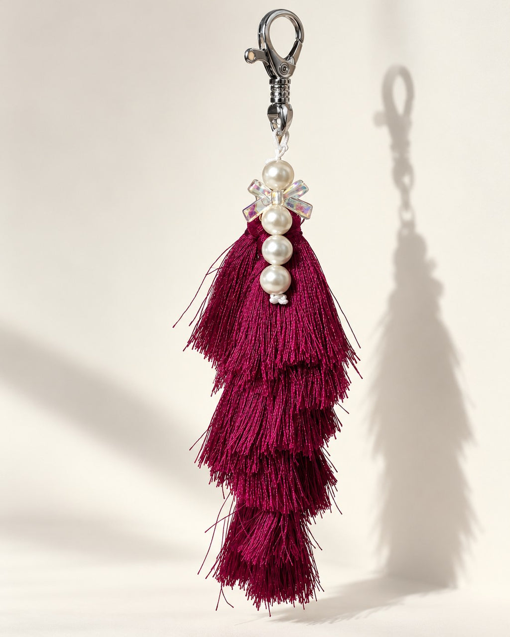 Gulabi silk tassel bag charm: a vertical strand of four white pearl beads with a small clear bow between the first and second, on a white tie cord. It hangs from a silver-tone swivel clasp.