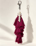 Gulabi silk tassel bag charm: a vertical strand of four white pearl beads with a small clear bow between the first and second, on a white tie cord. It hangs from a silver-tone swivel clasp.