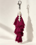 Gulabi silk tassel bag charm: a vertical strand of four white pearl beads with a small clear bow between the first and second, on a white tie cord. It hangs from a silver-tone swivel clasp.