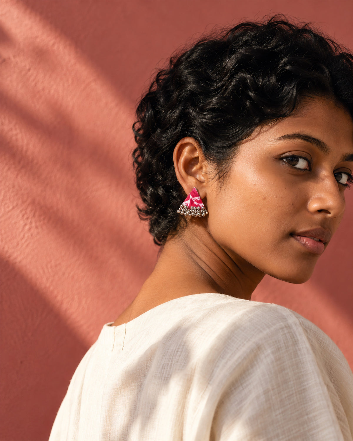 Riwaayat Noor Pink Triangle Earrings, worn in profile, cream top, terracotta pink wall