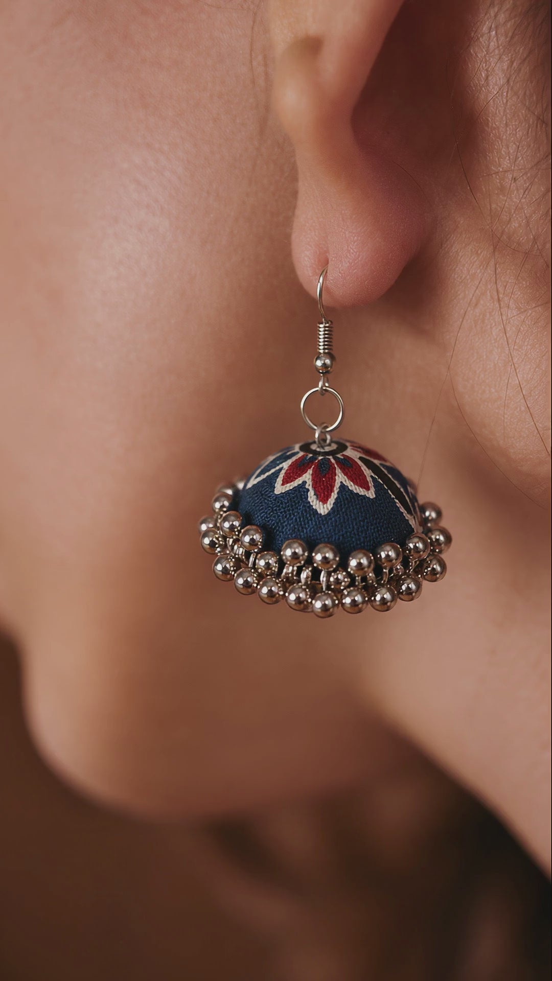 Laalbagh navy fabric jhumka with a red lotus and a silver bead fringe swaying gently on the ear (AI-generated styling video)