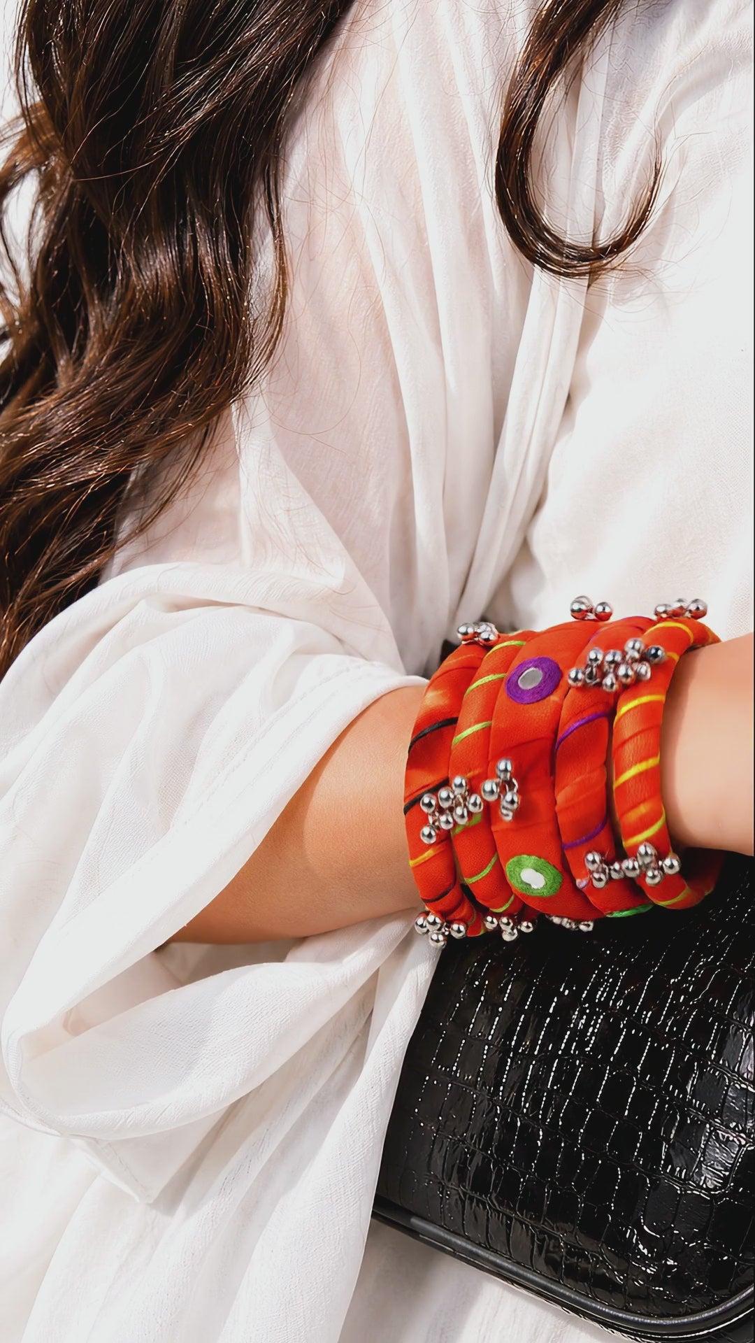 Rangriti orange fabric kada and four bangles with mirror work and ghungroo bells as the wrist moves slowly (AI-generated styling video)