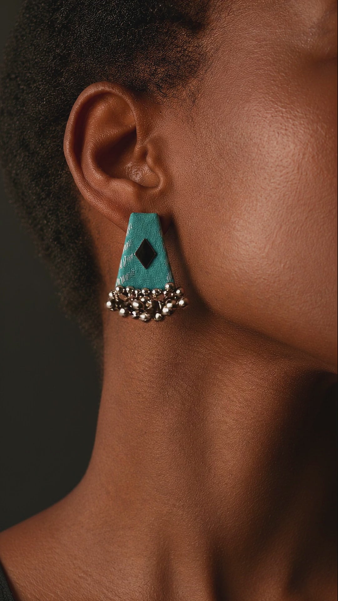 Kamal teal fabric drop earring with a black diamond motif and a fringe of small ghungroo bells, the bells moving gently (AI-generated styling video)