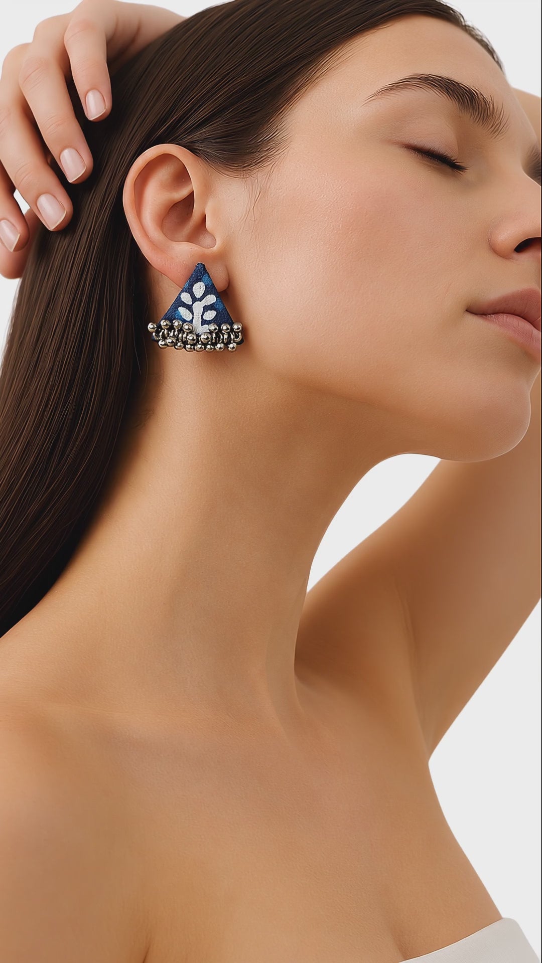 Blue and white block-print triangle fabric earrings with antique-silver ghungroo bells, worn as the model slowly tilts her head (AI-generated styling video)