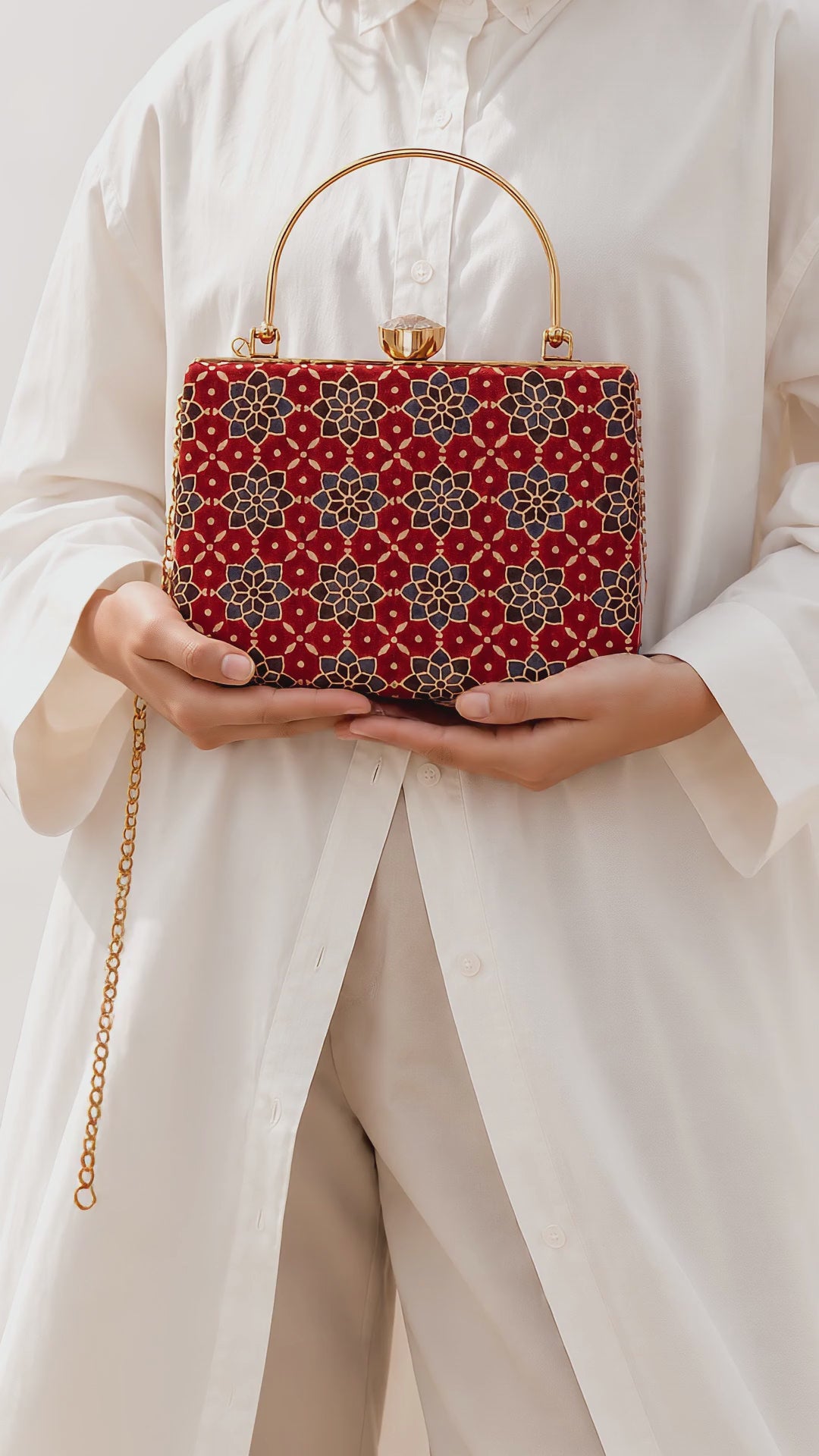 Laal Noor rectangular red Ajrakh Mashru silk handbag held in both hands against a white shirt, the gold chain swinging softly