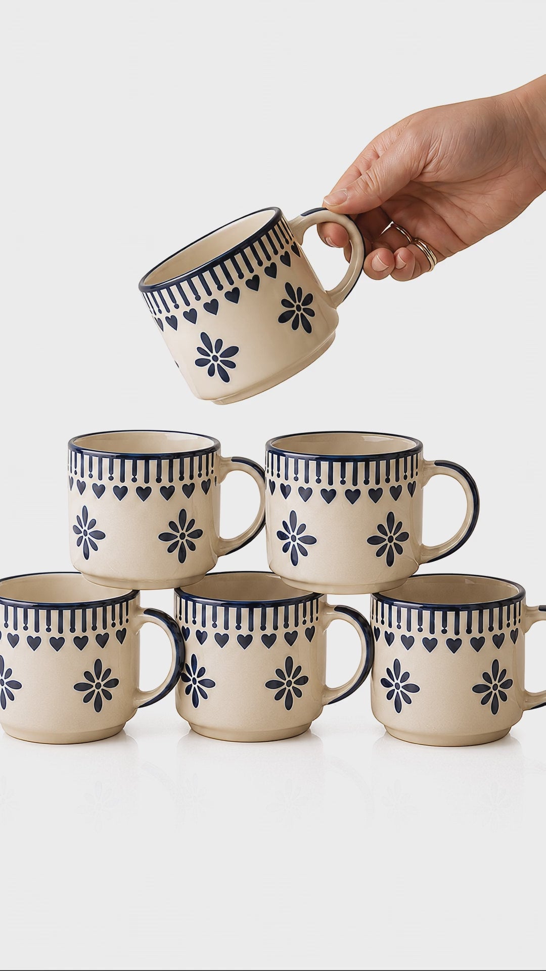 Saanjh hand-painted ivory and indigo ceramic cups, one lifted gently from the stack