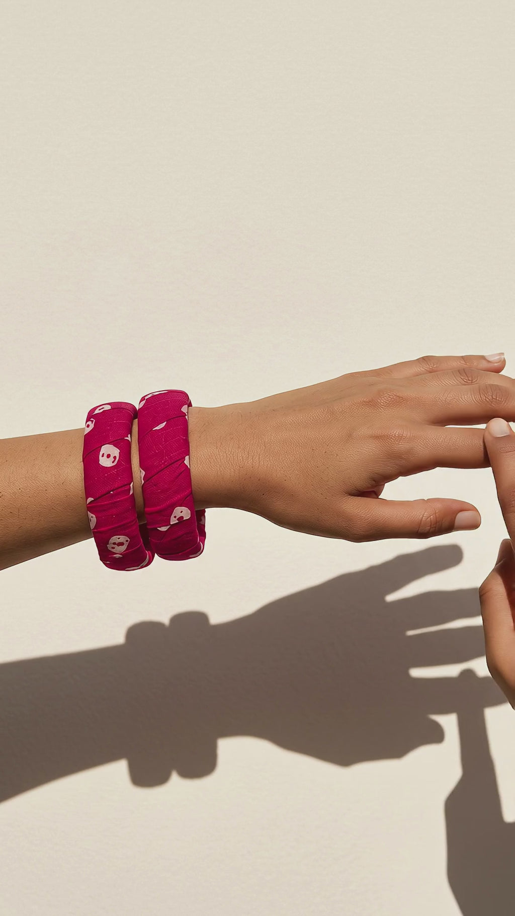 Gulnaar magenta pink floral fabric bangles on the wrist, the hand moving gently against a sunlit cream wall (AI-generated styling video)