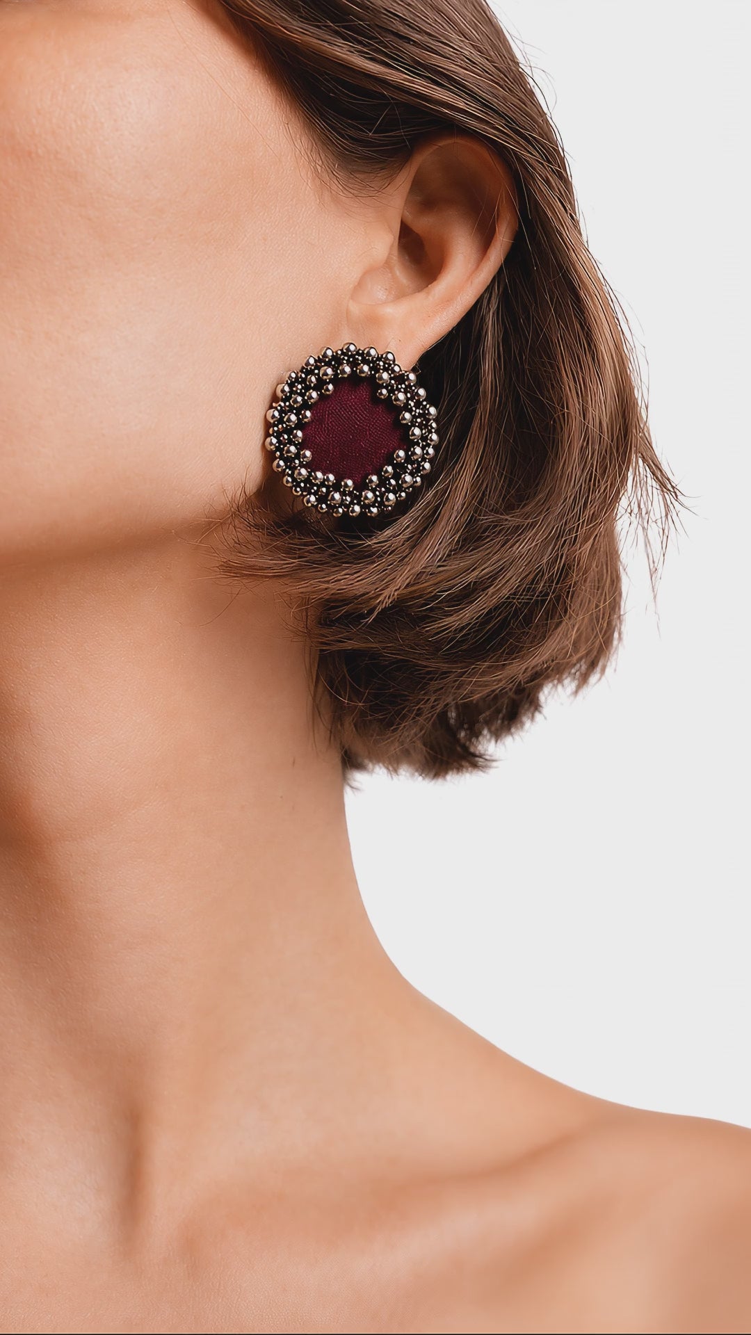Maroon ghungroo stud earrings ringed with tiny silver bells, worn as the model slowly turns her head (AI-generated styling video)