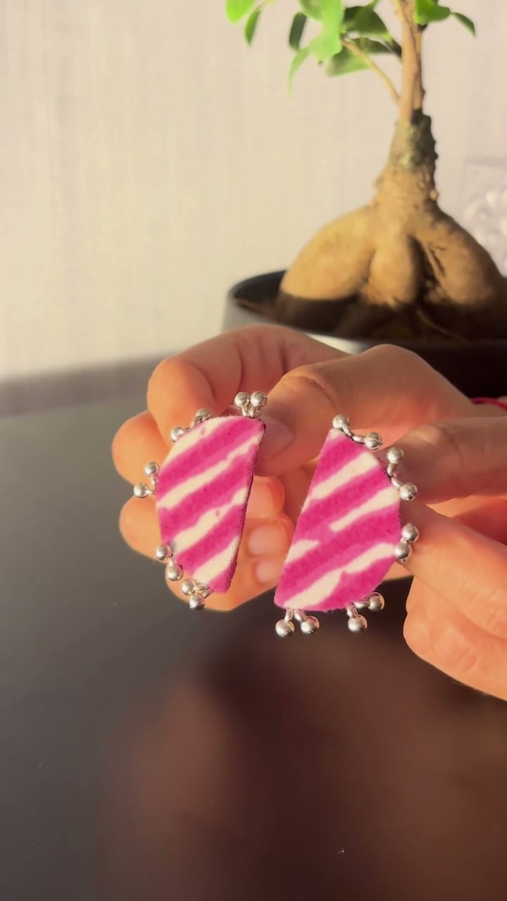 Leher Fuchsia Pink Half Moon Earrings: Leher Fuchsia Pink half moon earrings held between the fingers: fuchsia and white lehariya stripes edged with silver-tone ghungroo beads
