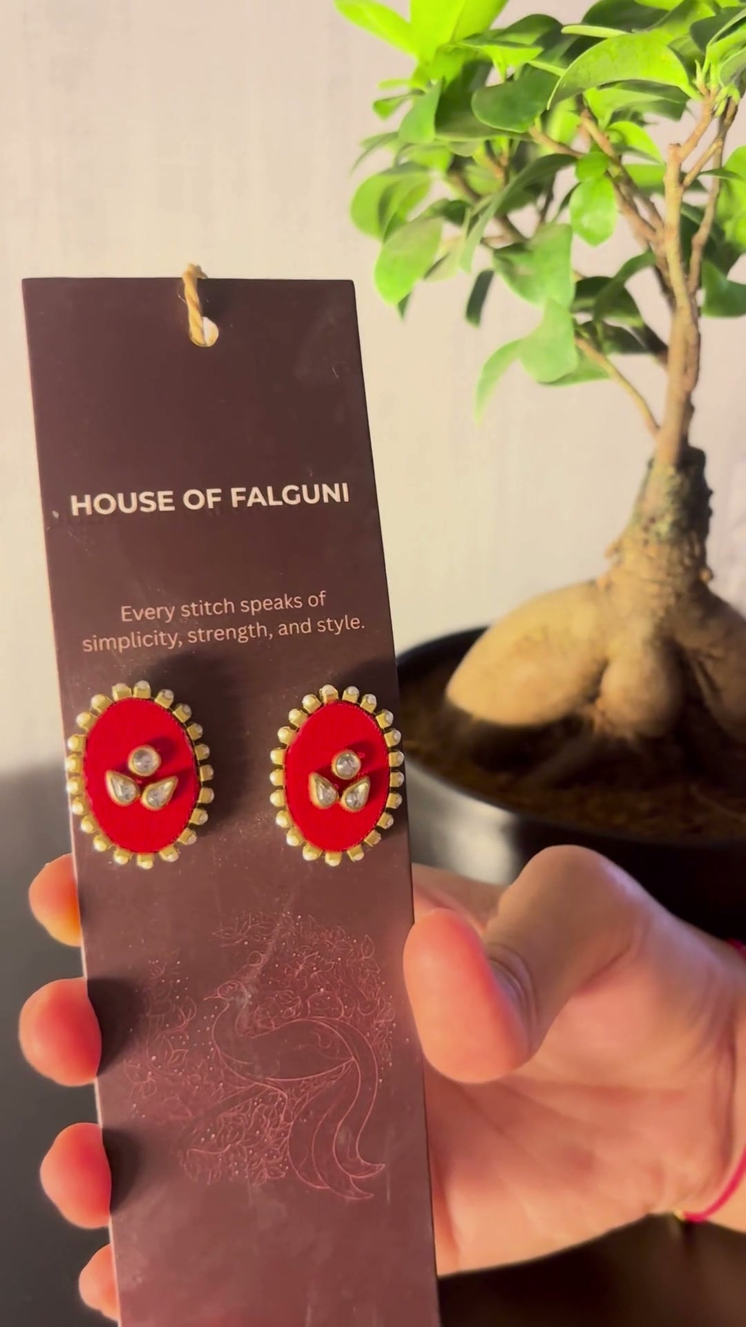 Mogra Red Oval Kundan Studs: Mogra Red Oval Kundan Studs on a House of Falguni card, tilted in the light: red oval fabric studs with three kundan stones and a small kundan border
