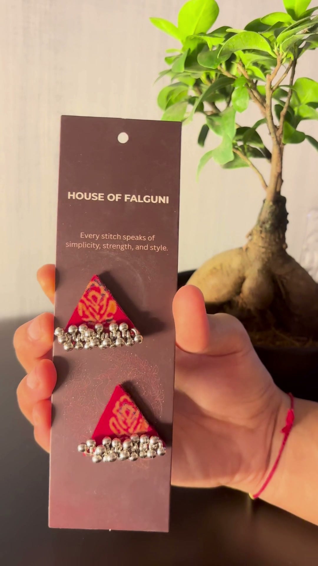 Riwaayat Gulnaar Red Triangle Earrings: Riwaayat Gulnaar red triangle earrings on a House of Falguni card, brought up close: red block print with an orange floral motif and a row of ghungroo bells