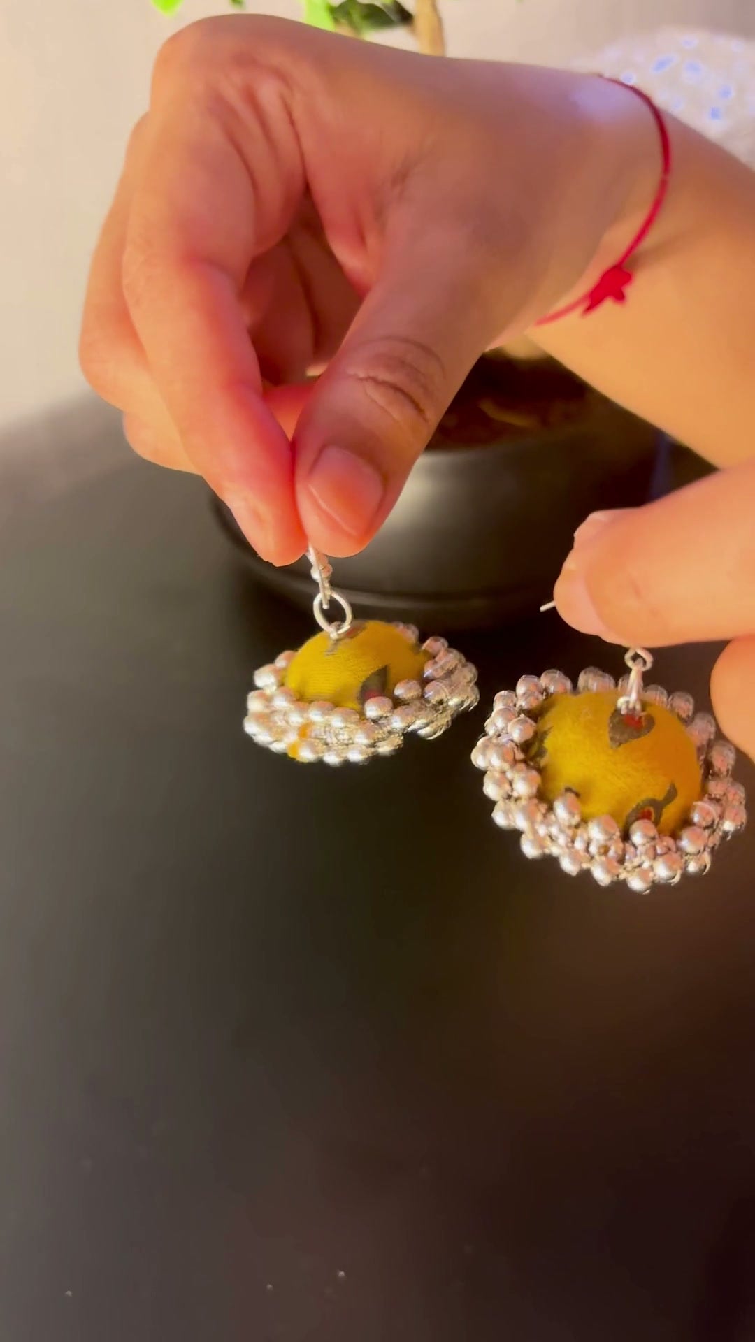 Mustard Jhumka Earrings: Mustard fabric jhumka earrings hung from the fingers: mustard yellow domes with small olive and grey leaf motifs and a ghungroo bell fringe