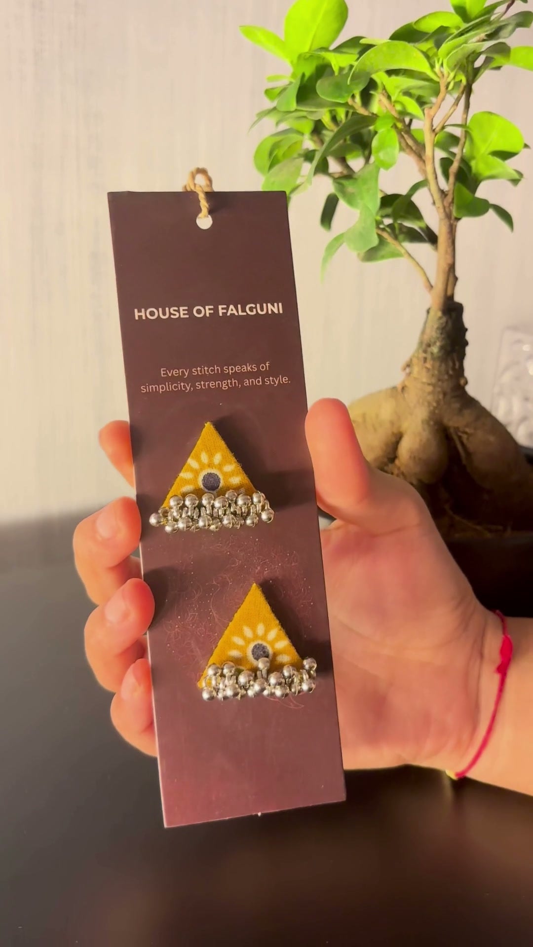 Riwaayat Kesar Mustard Triangle Earrings: Riwaayat Kesar mustard triangle earrings on a House of Falguni card, brought up close: mustard print around a small mirror and a row of ghungroo bells