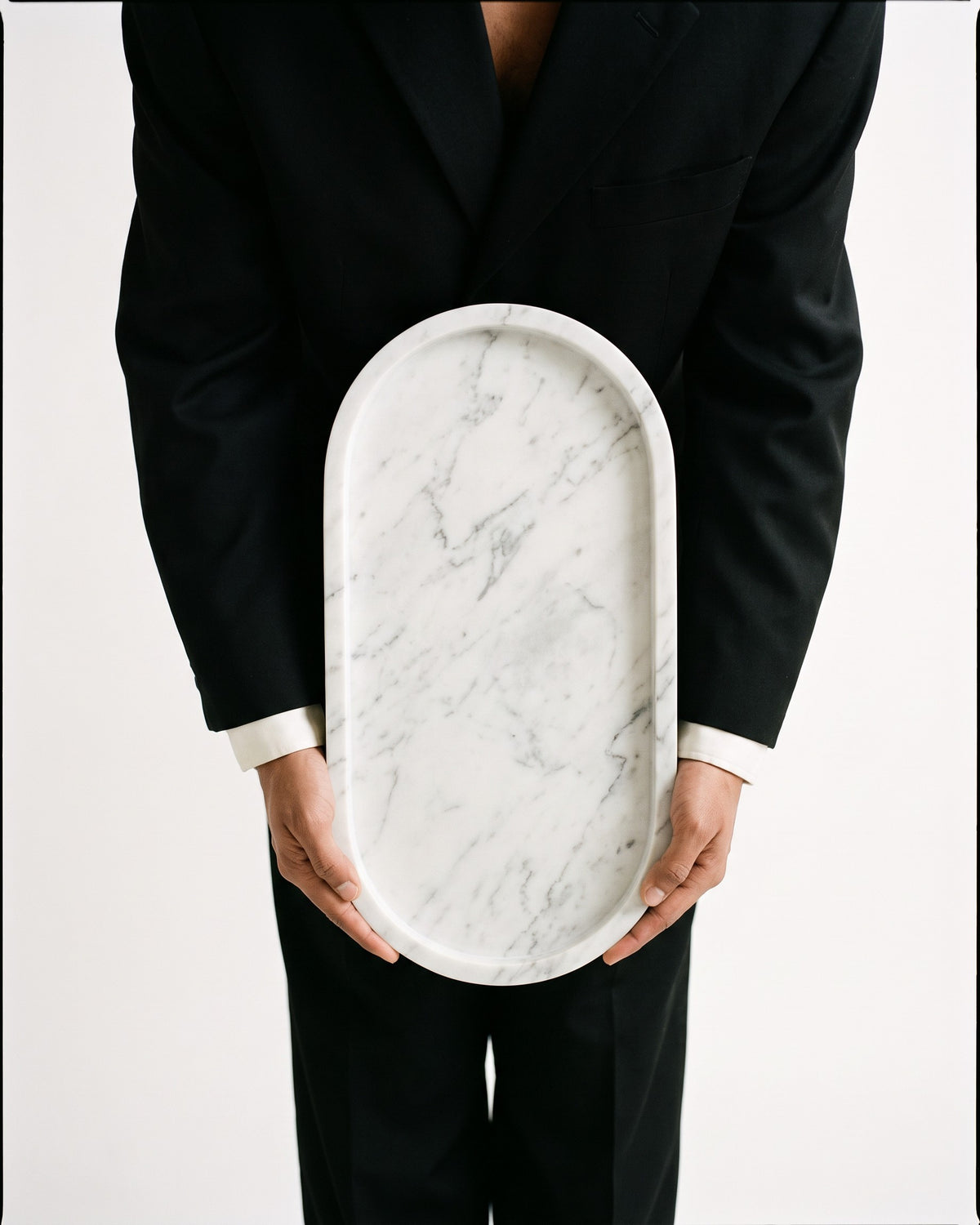 Quiet Table Marble Tray, Oval Serving & Vanity Tray held by a model in a black suit, bone-white studio