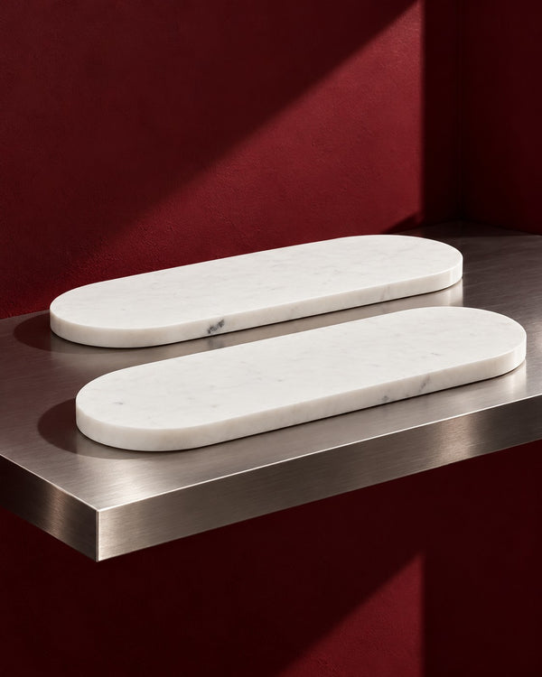 Quiet Table Marble Tray, Oval Serving & Vanity Tray two trays on a steel ledge against maroon (AI-generated styling image)