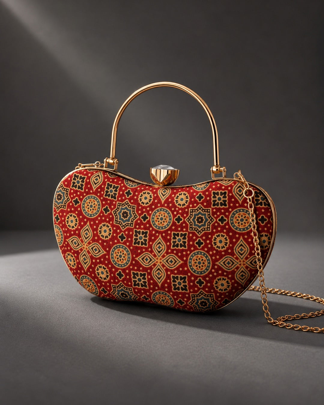 Rang Mahal Mashru silk handbag with a curved gold-tone frame, red ground printed with gold and teal medallions and eight-point stars, arched top handle and chain