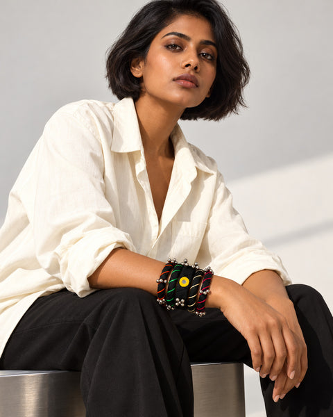 Rangriti black fabric kada and four bangles with mirror work and ghungroo, worn by seated model in an ivory shirt (AI-generated styling image)