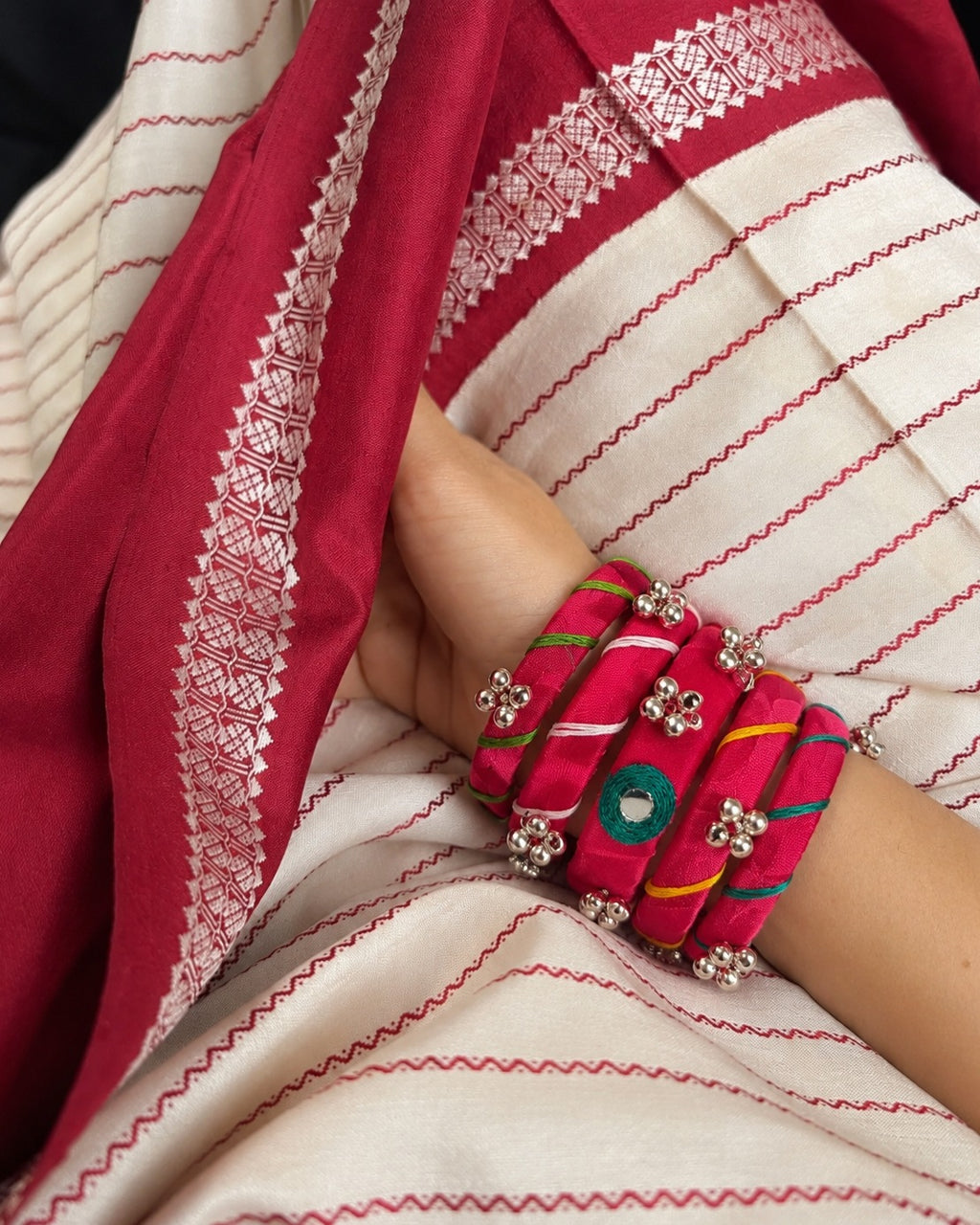 Rangriti pink mirror work bangles worn against a red and ivory striped saree