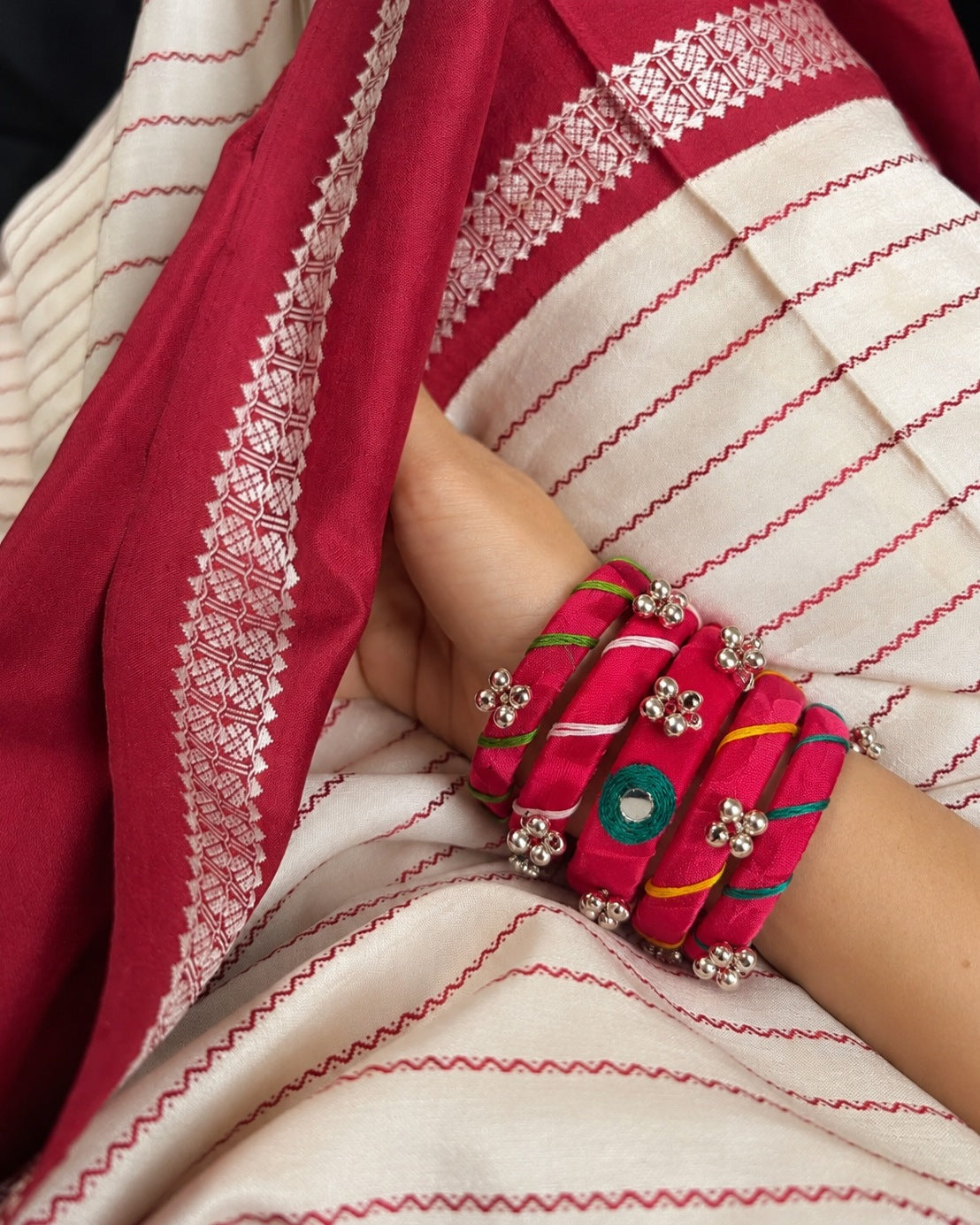 Rangriti pink mirror work bangles worn against a red and ivory striped saree