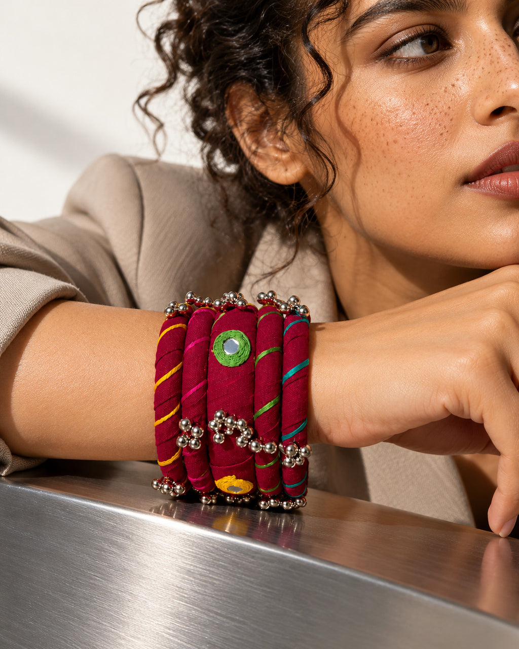 Rangriti maroon fabric kada and four bangles with mirror work and ghungroo, worn by model resting her wrist on steel (AI-generated styling image)