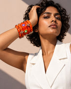 Rangriti orange fabric kada and four bangles with mirror work and ghungroo, worn by model in white tailoring (AI-generated styling image)
