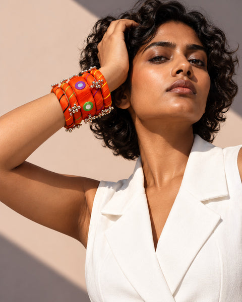 Rangriti orange fabric kada and four bangles with mirror work and ghungroo, worn by model in white tailoring (AI-generated styling image)