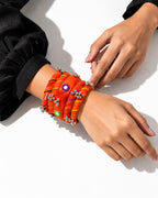 Rangriti orange fabric kada and four bangles with mirror work and ghungroo, overhead view on a model’s wrist (AI-generated styling image)