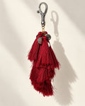 Raktima silk tassel bag charm: a cluster of embossed silver-tone coins at the head, above tiered ruby red silk tassels. It hangs from a silver-tone swivel clasp.
