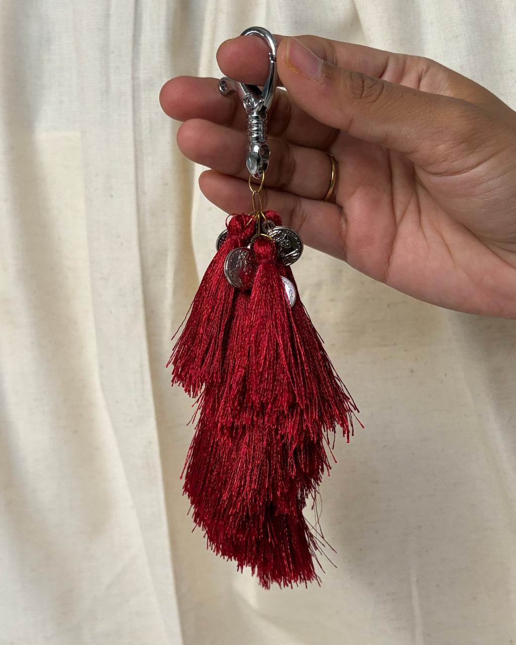 Raktima silk tassel bag charm held in the hand to show its size, about 9 inches from clasp to fringe