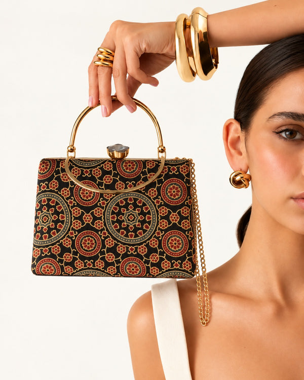 Ruhani black and maroon medallion handbag held up by its gold-tone arched handle beside the model's face