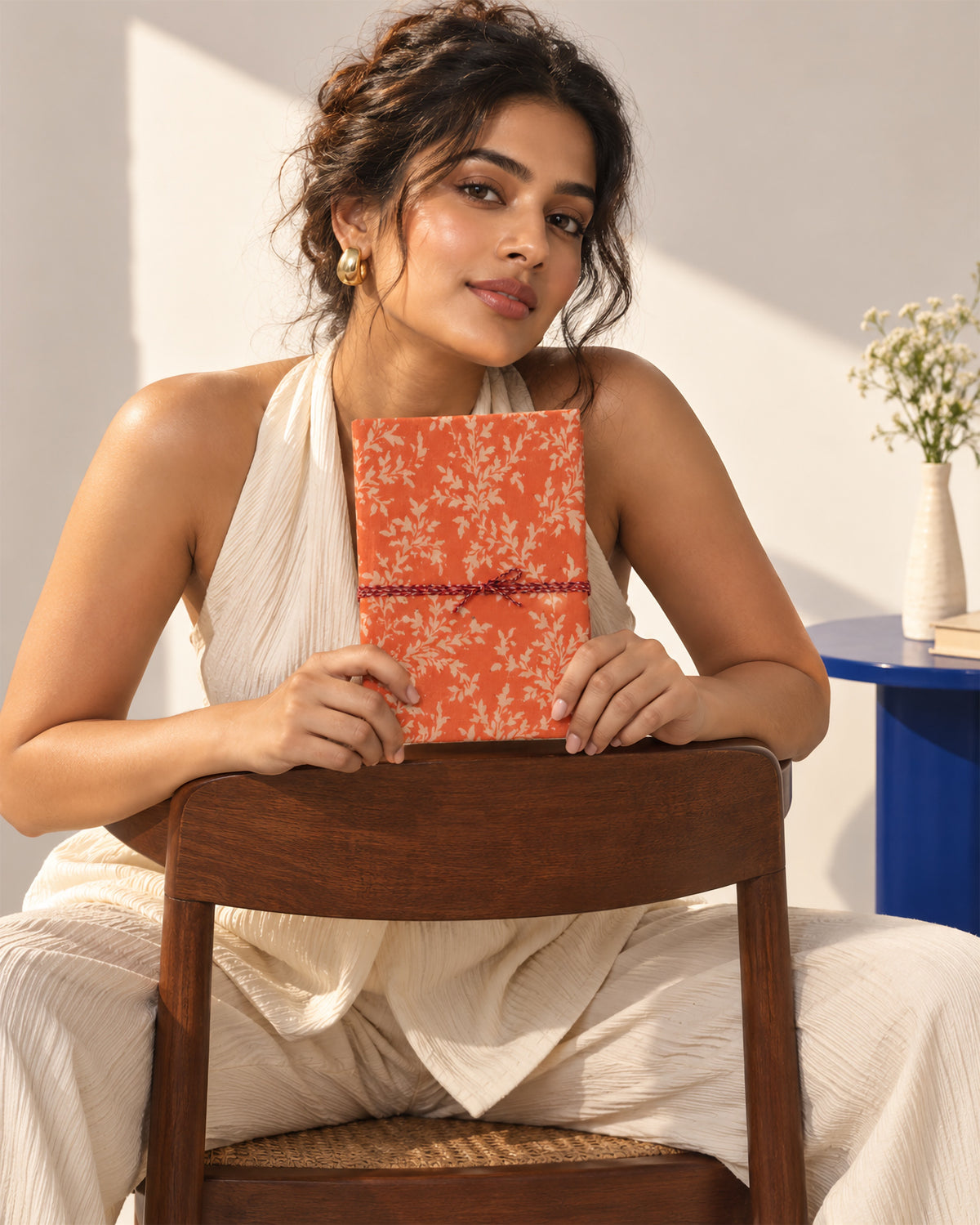 Saffron Bloom Block Print Fabric Diary, 200 Unruled Pages, held at the chest, seated on a chair, white outfit