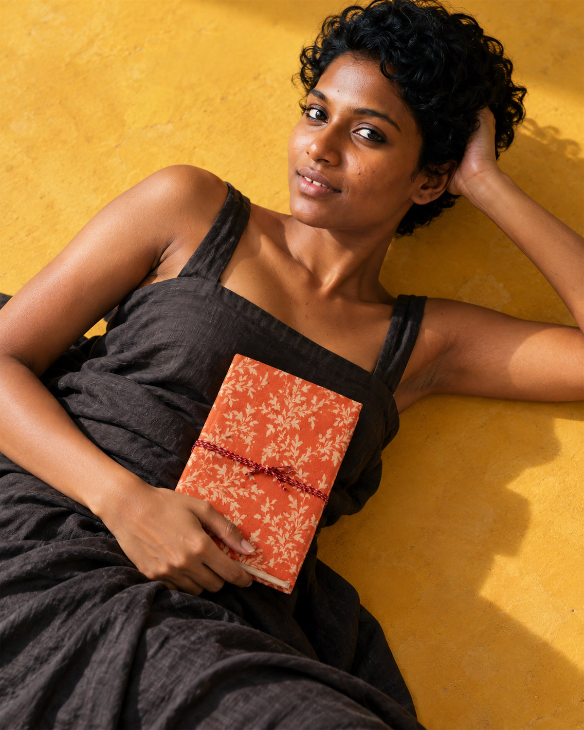 Saffron Bloom Block Print Fabric Diary, 200 Unruled Pages, held at the chest, black dress, saffron yellow wall