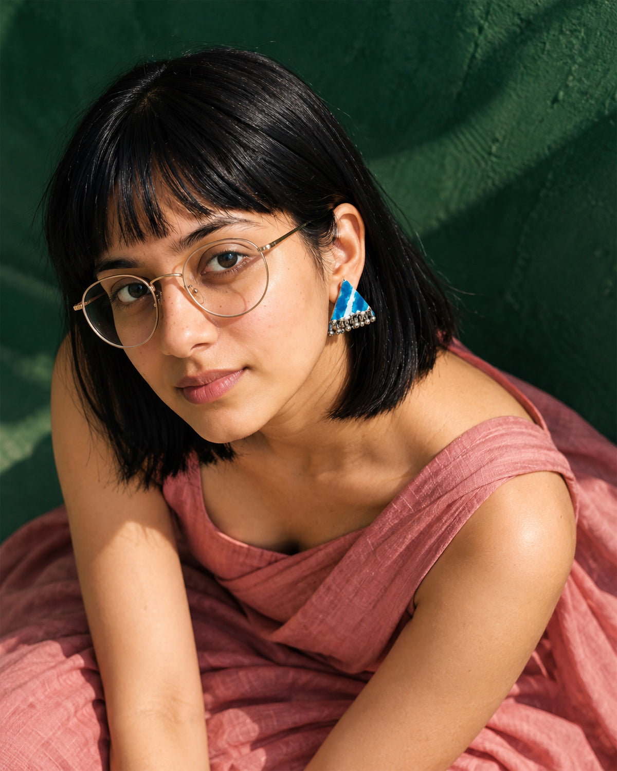 Riwaayat Neelambara Sky Blue Triangle Earrings, worn, round glasses, pink top, deep emerald wall