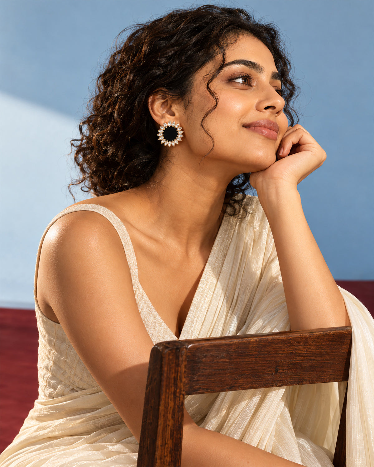 Black Floral Kundan Earrings, worn, hand at the cheek, sky blue wall