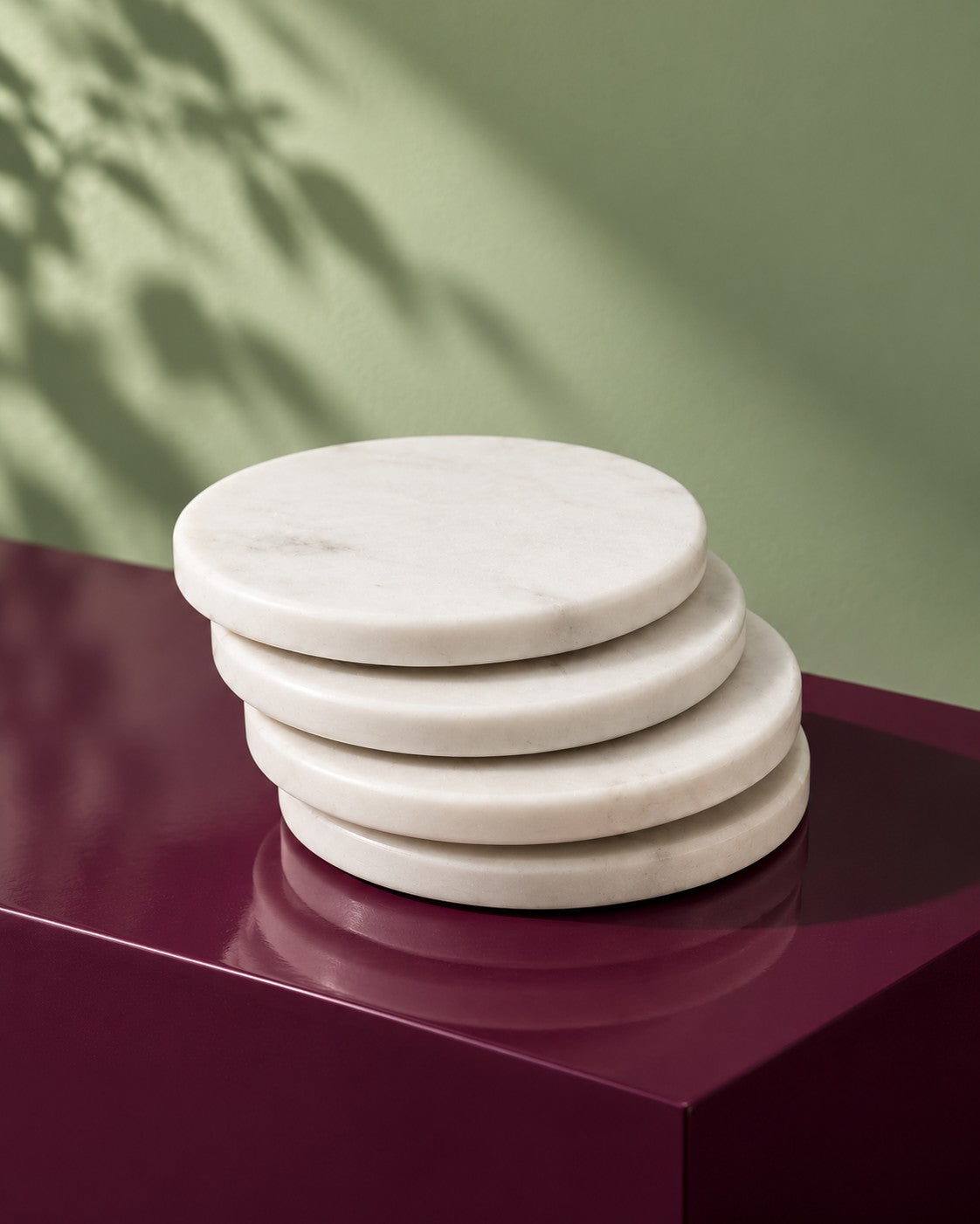 Table Companions, Hand-Carved Marble Coasters (Set of 4) four coasters stacked on a maroon plinth in dappled light