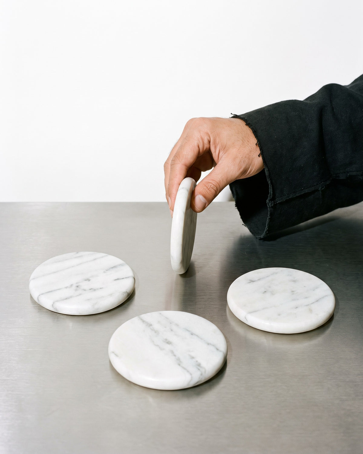 Table Companions, Hand-Carved Marble Coasters (Set of 4) four coasters on a steel table, one lifted by hand