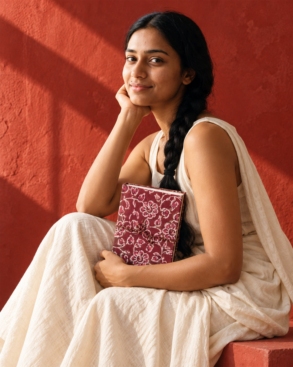 Wine Suzani Block Print Fabric Diary, 200 Unruled Pages, held at the chest, white outfit, vermilion red wall